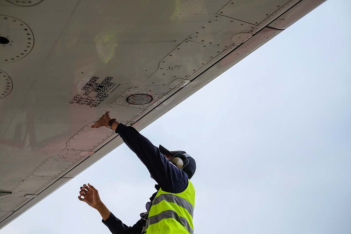 airplane wing man in green safety vest standing under white structure wing